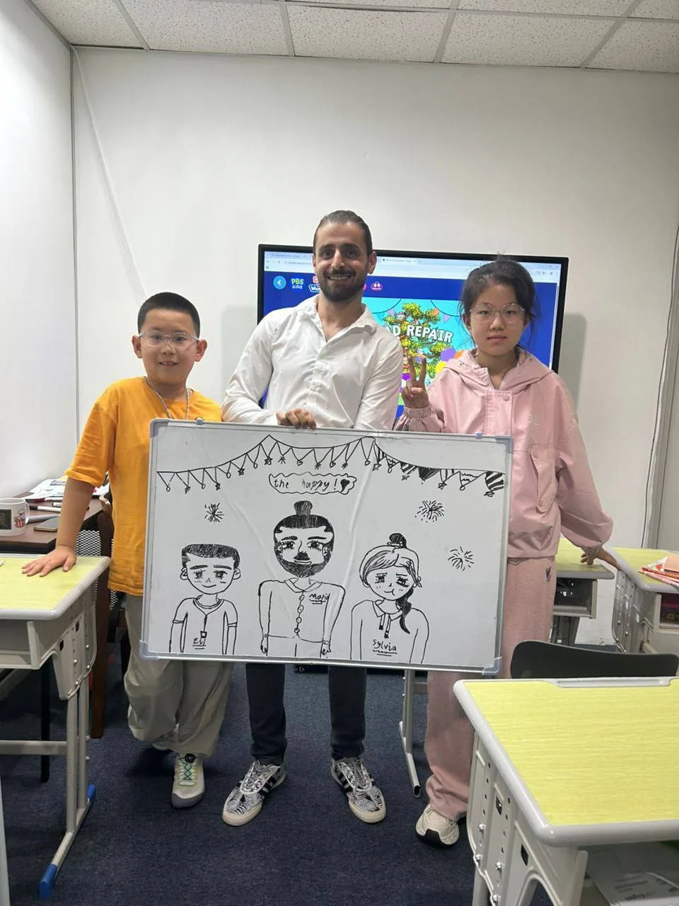 A teacher and two young students holding a whiteboard with their own drawings.