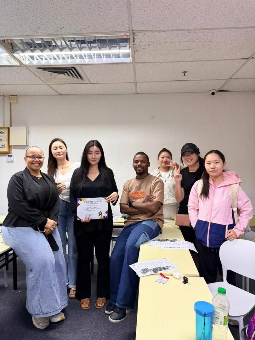 A group of adult students and teachers with a completion certificate in the classroom.