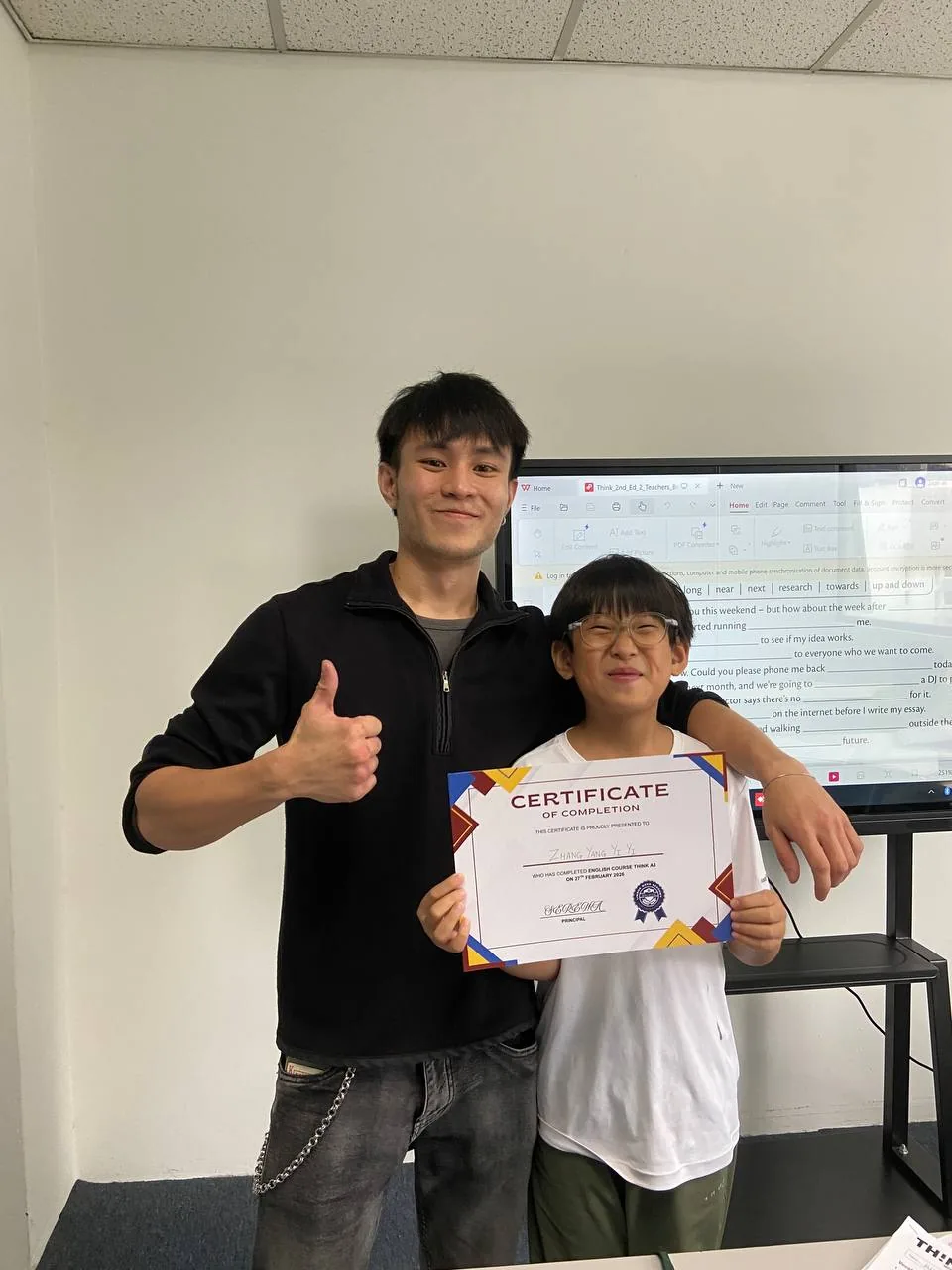 A young student proudly holding a course completion certificate with a teacher.