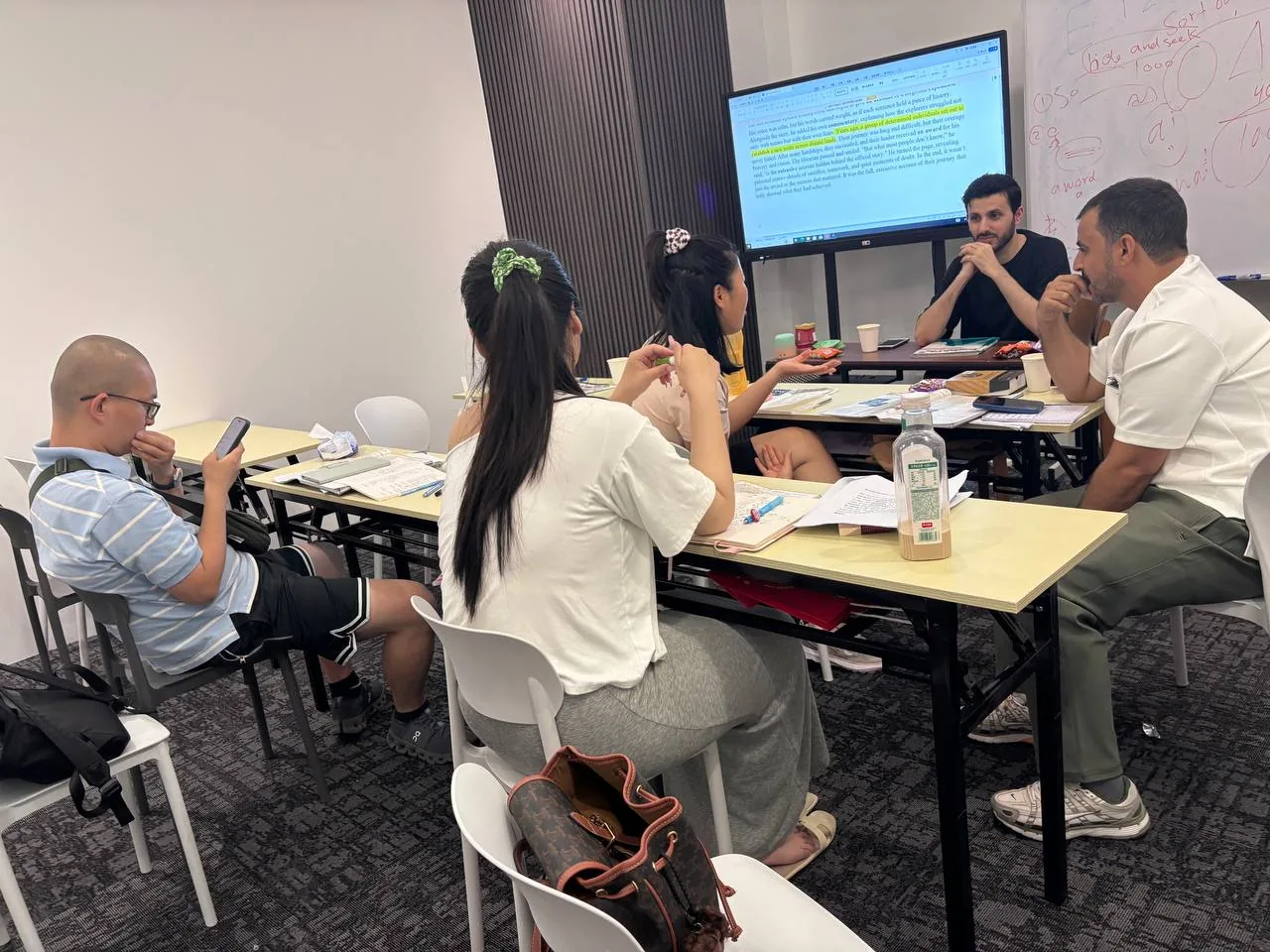 Adult students in a reading lesson with a teacher and an on-screen text.