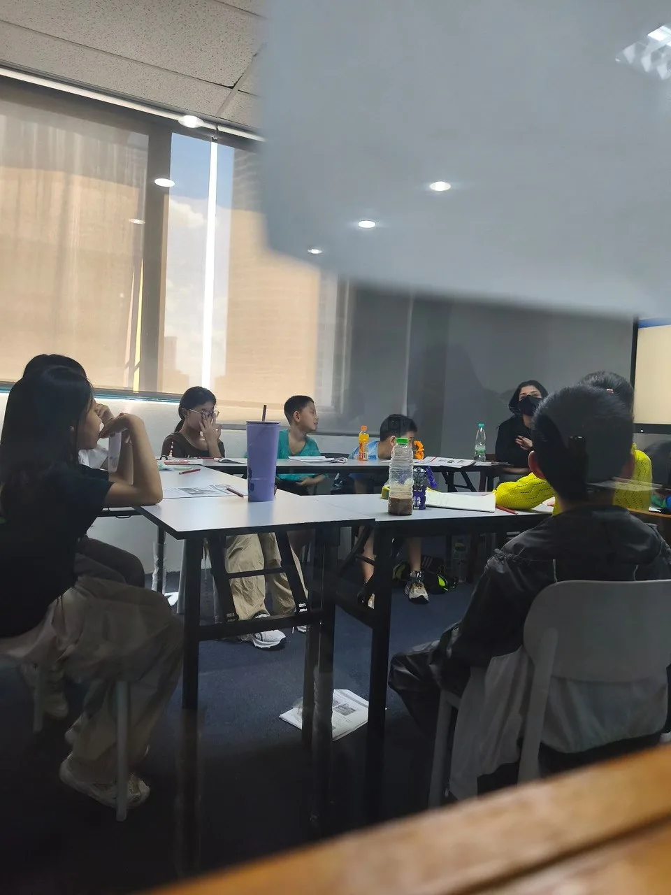 A candid view of a class of students seated at tables during a lesson.